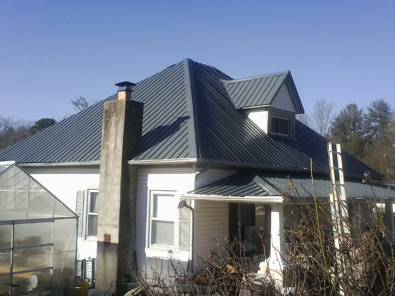 Dark blue standing seam metal roof on a white farmhouse with dormer — Slate & Tile Roof Repair by Roofing Brothers in Becket
