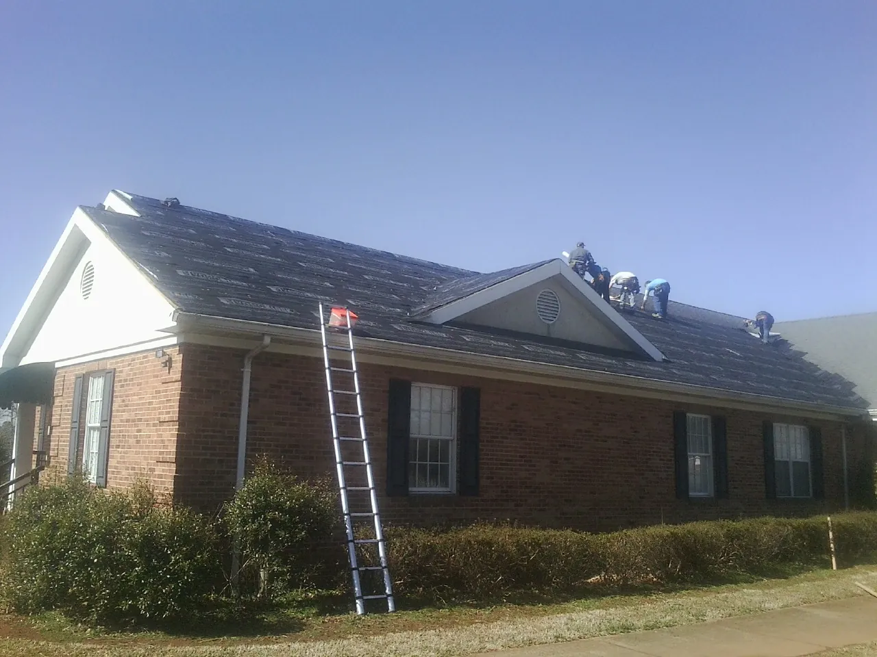 Crew tearing shingles off a brick ranch roof with a ladder set — Emergency Roof Repair work by our crew in Becket