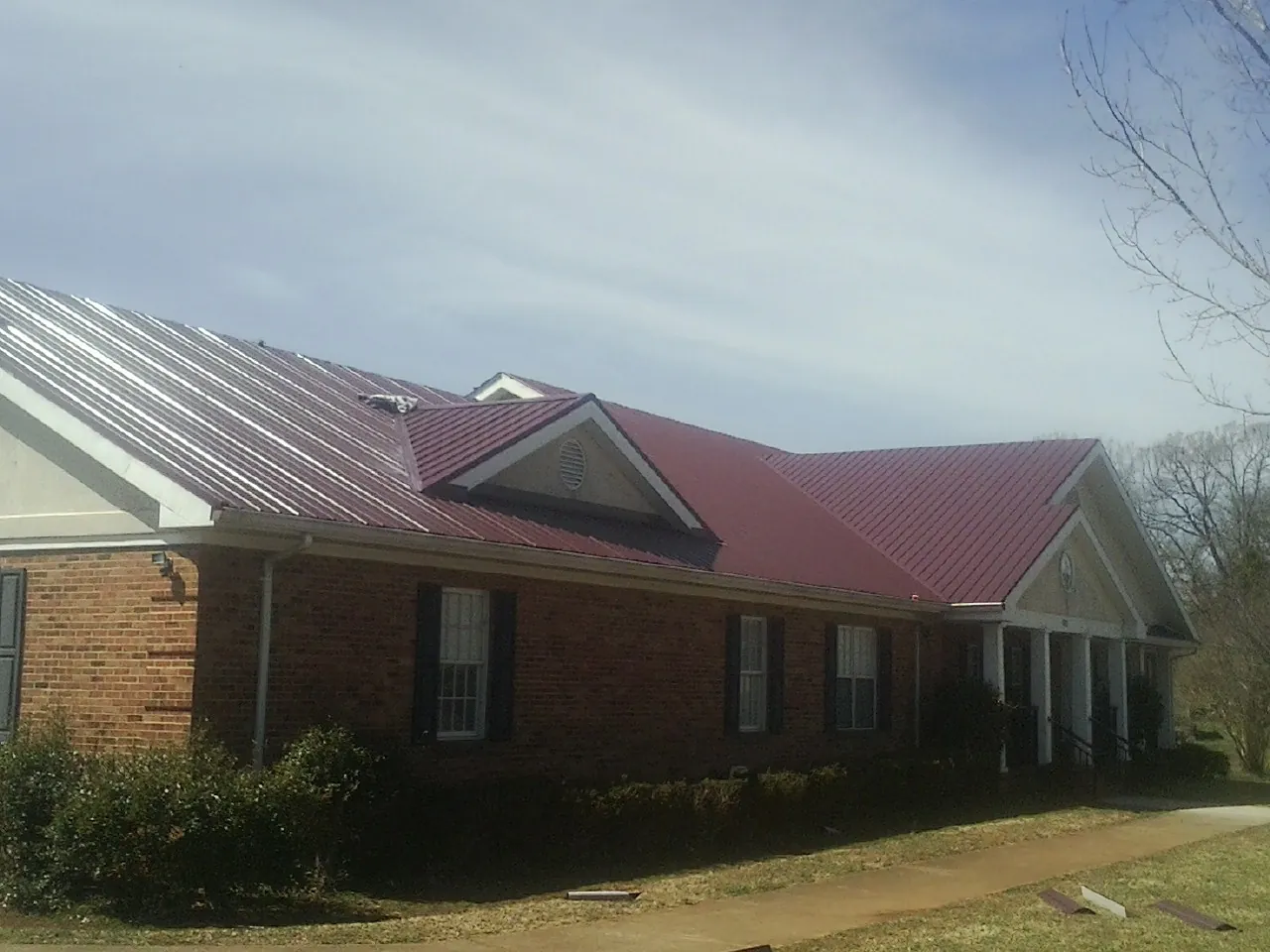 Red metal roof with gabled entries on a long brick building, from a Hail Damage Roof Repair job in Becket