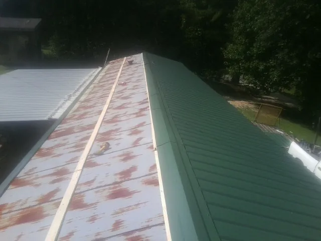 Old rusted panels beside newly installed green metal roofing — Wind Damage Roof Repair by Roofing Brothers in Becket