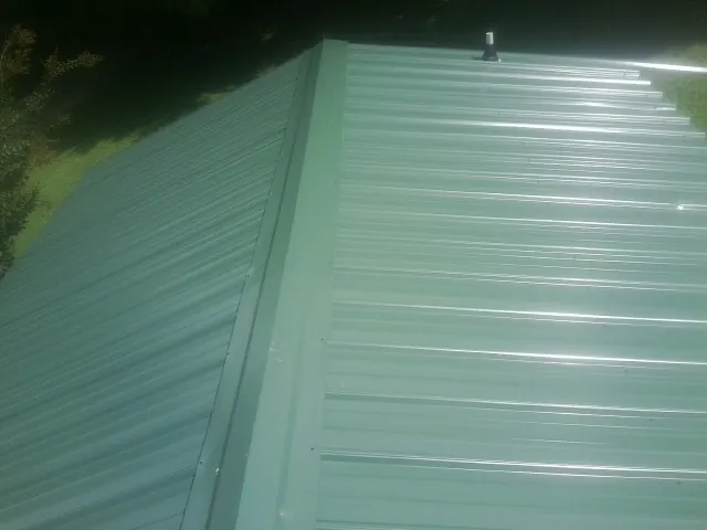 New green metal panels meeting at the ridge of a roof — Flat Roof Repair work by our crew in Becket