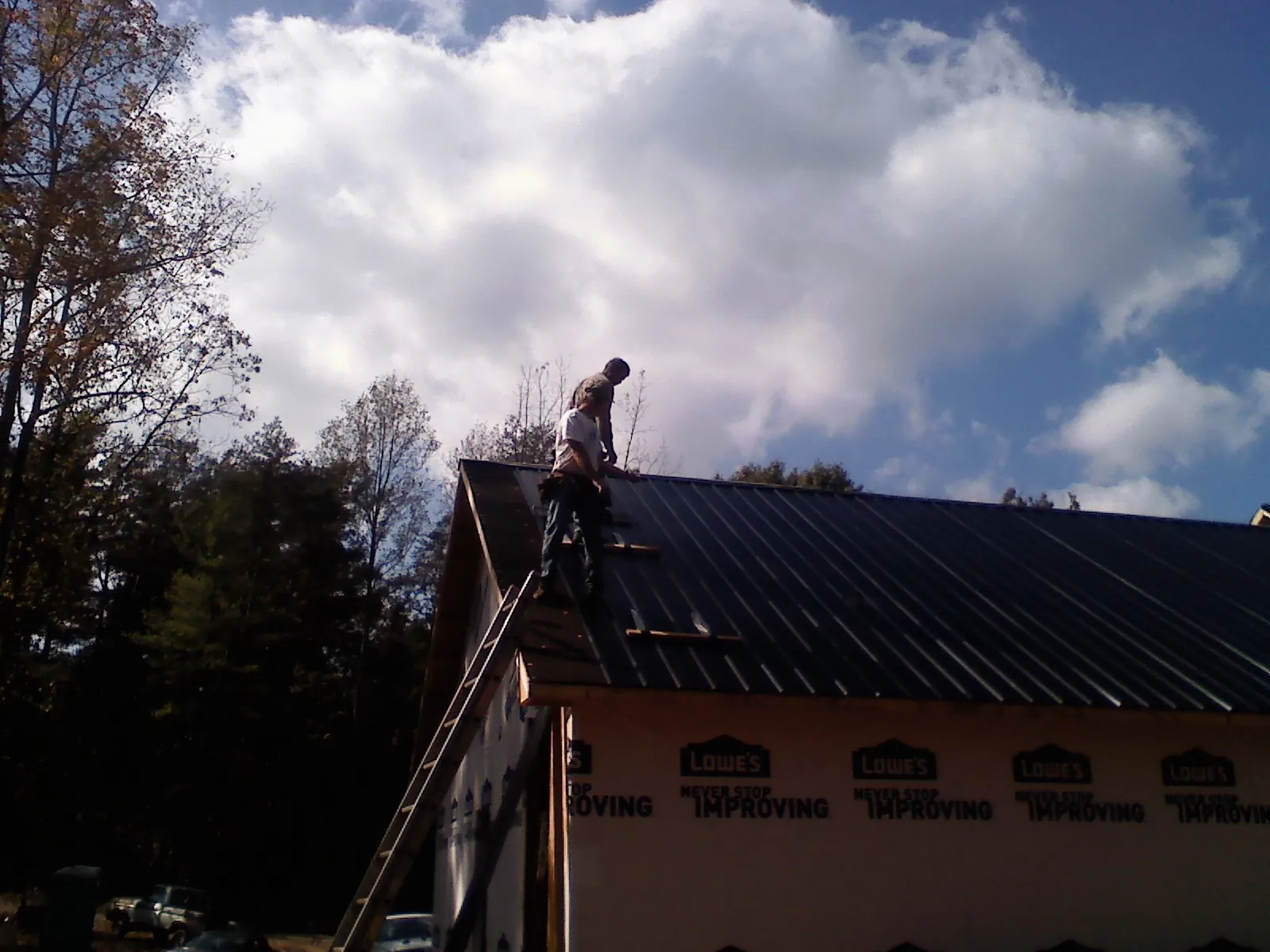 Roofer fastening dark metal panels high against a cloudy sky, from a Roof Inspection job in Becket
