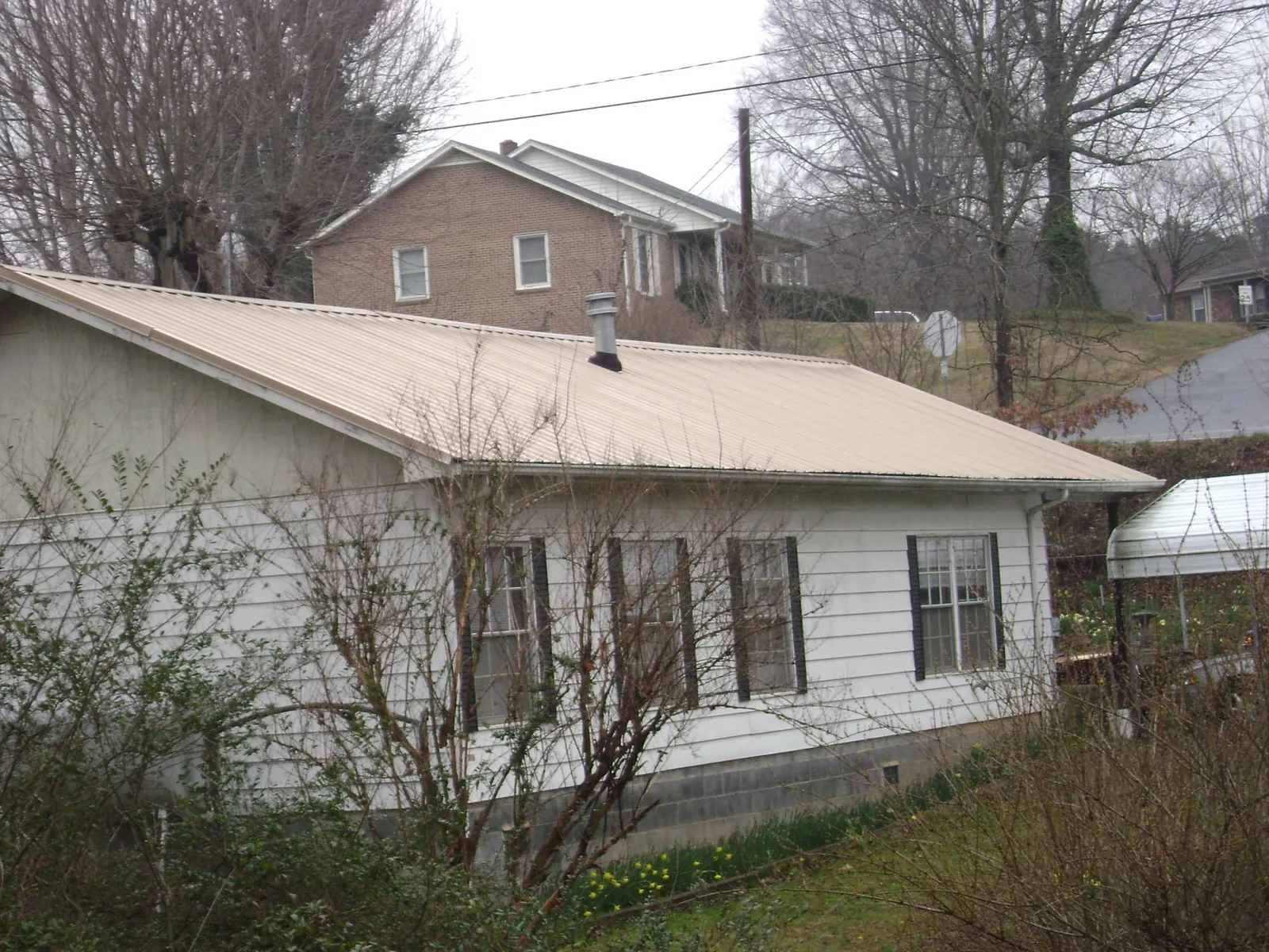 Tan metal roof on a white sided house set into a hillside — Commercial Roofing by Roofing Brothers in Becket