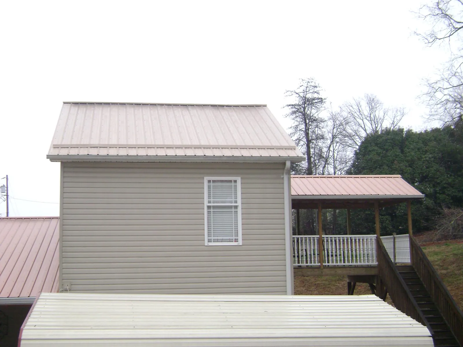Tan metal roofs on a two story addition and attached porch, from a Roof Replacement job in Becket
